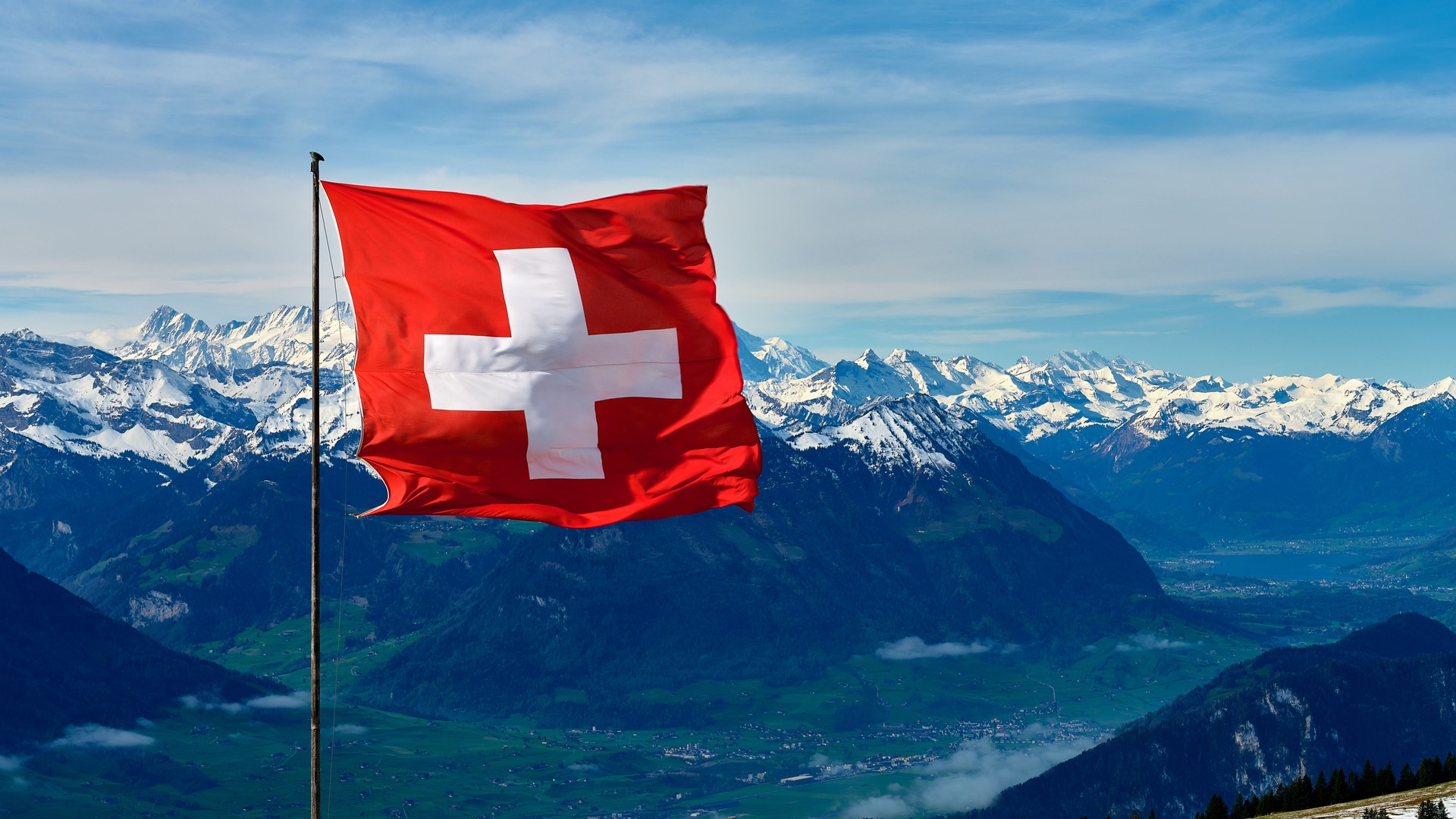 Beautiful Swiss flag waving against the backdrop of snow-capped mountains and clear blue skies in a serene Alpine landscape